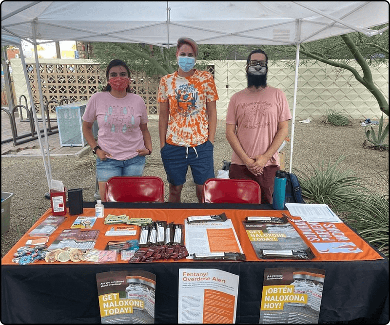Three SPW staff members stand at a table at an event. The table has lots of SPW supplies, brochures, posters, and other information on it.